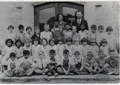 First grade class in 1929 seated outside of school with teacher Xenia Voigt