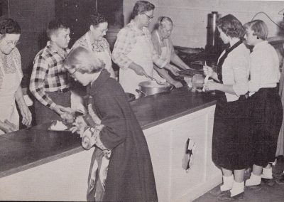 Lunch line showing six women and one younger male student serving food from pots to two female students